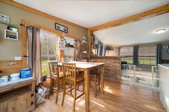 dining room featuring vaulted ceiling with beams, wood finished floors, and a textured ceiling