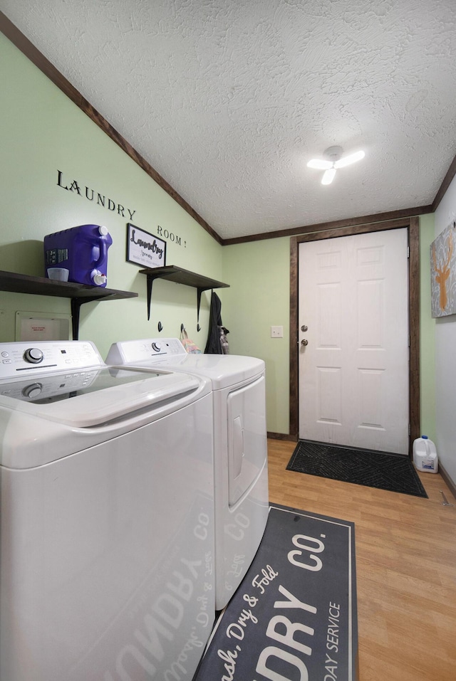 clothes washing area with wood finished floors, a textured ceiling, washing machine and dryer, ornamental molding, and laundry area
