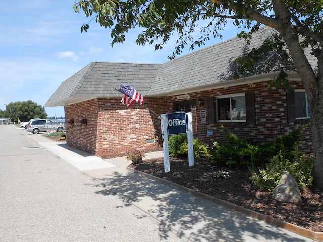 exterior space featuring brick siding, roof with shingles, and mansard roof