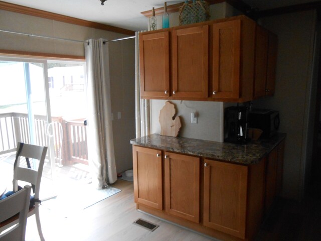 kitchen with brown cabinets, dark stone countertops, visible vents, black microwave, and light wood-type flooring