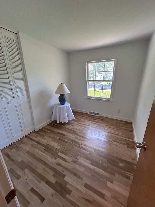 unfurnished bedroom with visible vents, baseboards, wood finished floors, and a closet