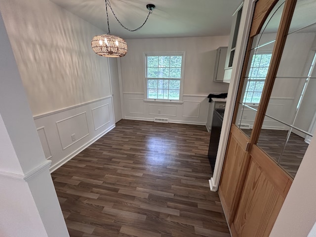 unfurnished dining area with visible vents, dark wood-style flooring, a decorative wall, a wainscoted wall, and a notable chandelier