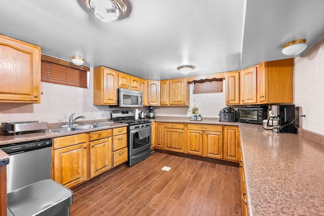 kitchen with dark wood finished floors, a toaster, stainless steel appliances, a sink, and tasteful backsplash