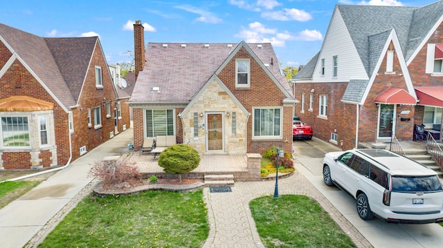 english style home with stone siding, a chimney, and brick siding