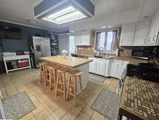 kitchen featuring stainless steel appliances, a sink, light tile patterned floors, and white cabinets