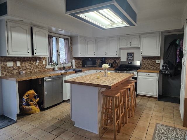 kitchen featuring stainless steel appliances, light tile patterned floors, white cabinets, a sink, and backsplash