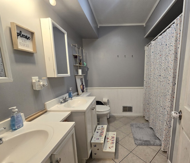 full bath featuring ornamental molding, a wainscoted wall, tile patterned floors, toilet, and two vanities