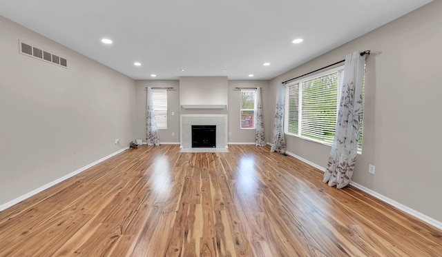 unfurnished living room featuring visible vents, baseboards, recessed lighting, a tiled fireplace, and light wood finished floors