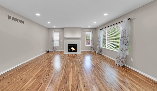unfurnished living room featuring light wood-style flooring, recessed lighting, baseboards, a tile fireplace, and visible vents
