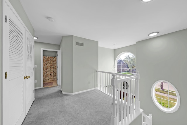 hallway with carpet flooring, baseboards, visible vents, and an upstairs landing