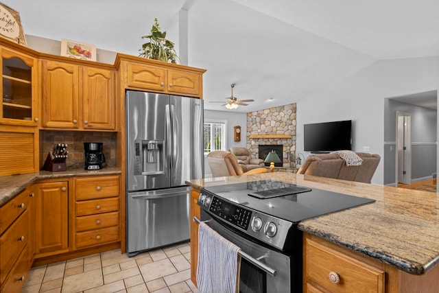 9681 Sugar Bush Run, Traverse City, MI 49685 - kitchen featuring a ceiling fan, a stone fireplace, light stone counters, appliances with stainless steel finishes, and lofted ceiling