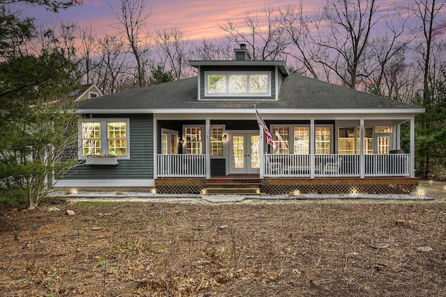 back of property at dusk featuring french doors, a porch, a chimney, and a shingled roof