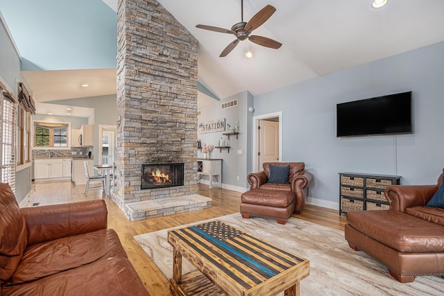 living area with light wood finished floors, a stone fireplace, visible vents, and a ceiling fan