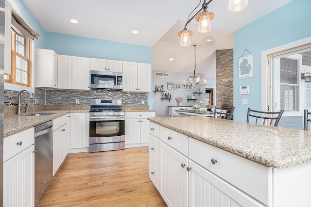 kitchen featuring light wood finished floors, stainless steel appliances, a sink, visible vents, and backsplash