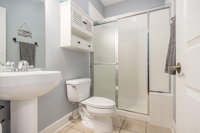 bathroom with toilet, a sink, a stall shower, baseboards, and tile patterned flooring