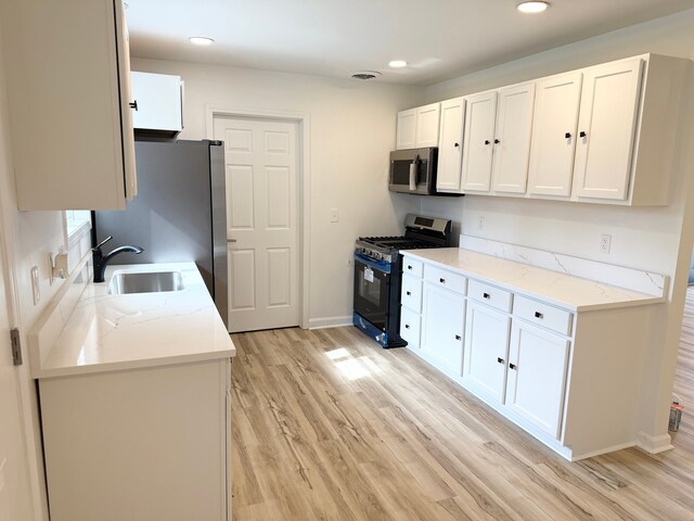 kitchen with light stone counters, a sink, light wood finished floors, white cabinetry, and appliances with stainless steel finishes