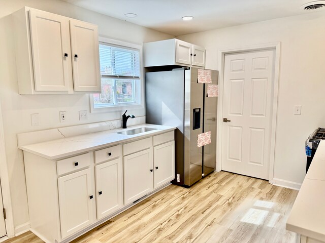 kitchen featuring light wood finished floors, stainless steel fridge with ice dispenser, visible vents, a sink, and white cabinetry