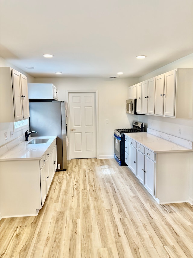 kitchen with light wood finished floors, a sink, baseboards, light stone countertops, and appliances with stainless steel finishes