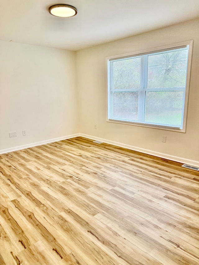 spare room featuring wood finished floors, visible vents, and baseboards