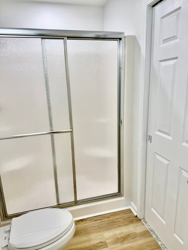 full bathroom with wood finished floors, a shower with shower door, and toilet