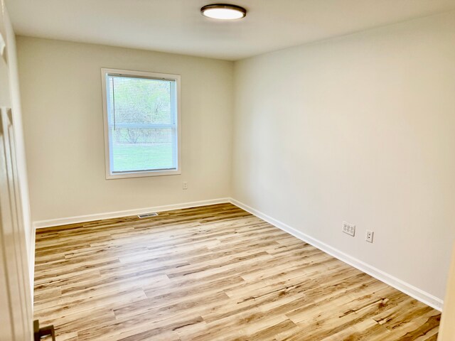 empty room with wood finished floors, visible vents, and baseboards