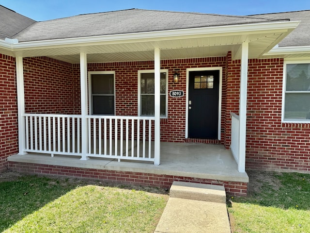 doorway to property with brick siding, a porch, and a shingled roof