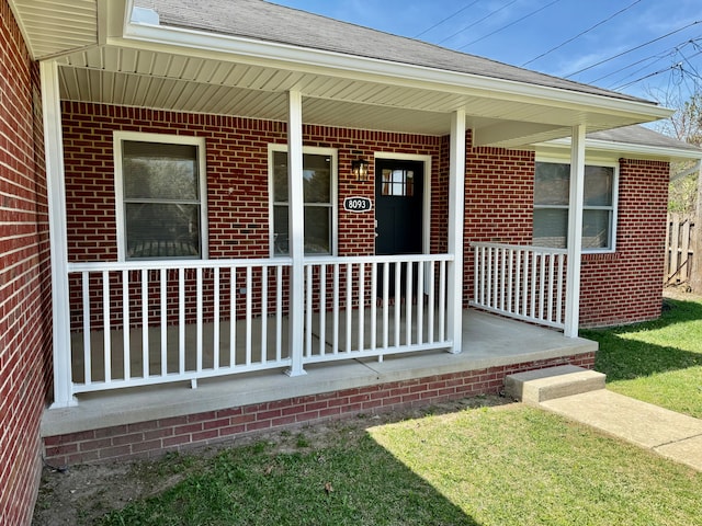 property entrance featuring covered porch, brick siding, and roof with shingles