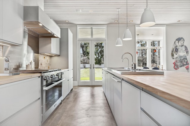kitchen featuring wall chimney range hood, decorative backsplash, high end stove, concrete flooring, and white cabinets