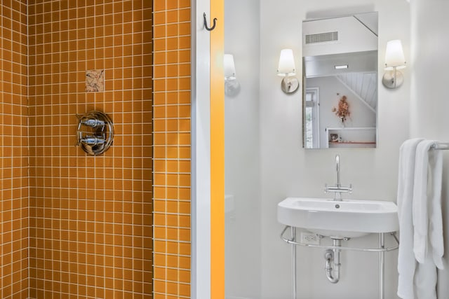 bathroom featuring visible vents, a sink, and tiled shower