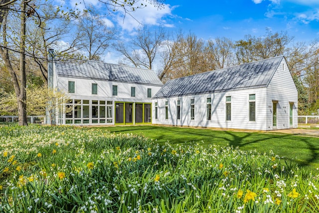 back of house featuring a sunroom, a yard, a chimney, and metal roof