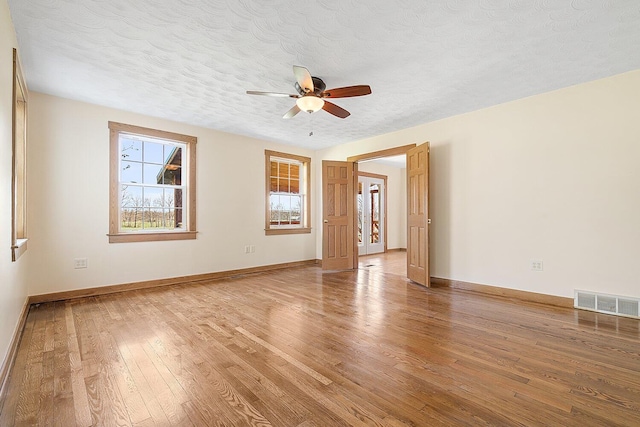 empty room featuring light wood-style flooring, visible vents, a wealth of natural light, and ceiling fan