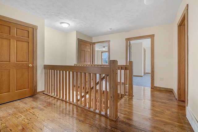 hall with baseboards, an upstairs landing, a textured ceiling, and hardwood / wood-style floors