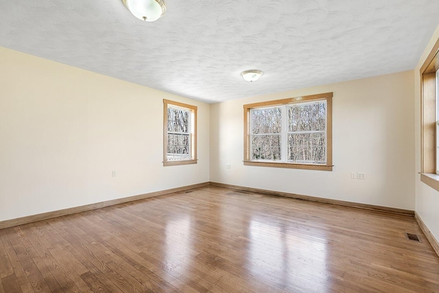 empty room featuring baseboards, wood finished floors, visible vents, and a textured ceiling