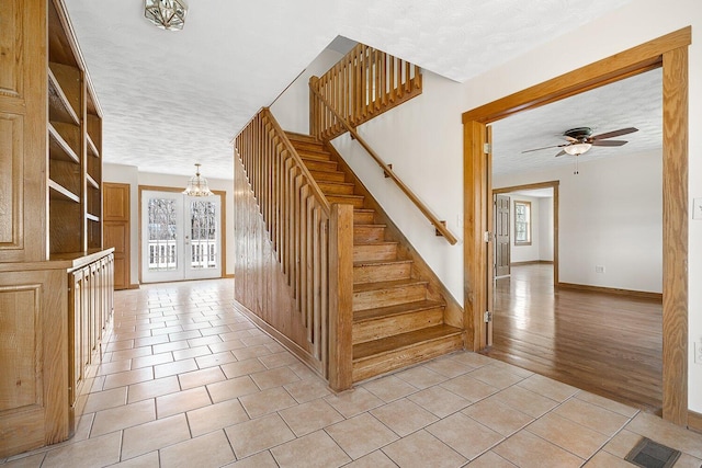 staircase featuring tile patterned floors, a textured ceiling, visible vents, and ceiling fan with notable chandelier