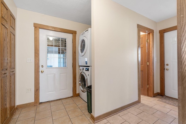 clothes washing area with baseboards, light tile patterned flooring, stacked washer and clothes dryer, and laundry area