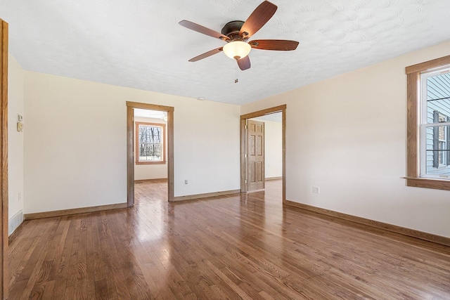 unfurnished room with wood finished floors, a textured ceiling, a ceiling fan, and baseboards