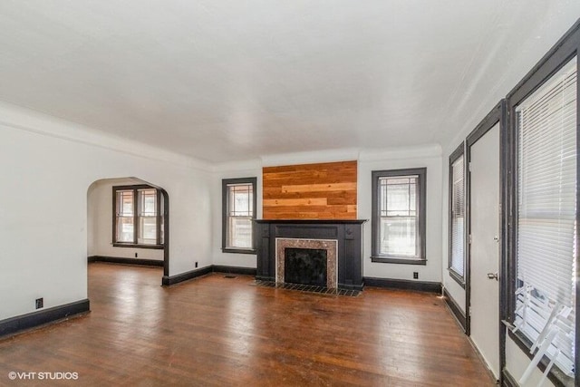 unfurnished living room featuring arched walkways, a fireplace with flush hearth, wood finished floors, and plenty of natural light