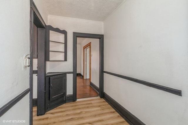 hall featuring light wood-type flooring, ornamental molding, and a textured ceiling