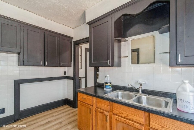 kitchen featuring a textured ceiling, light wood-style flooring, a sink, dark countertops, and backsplash