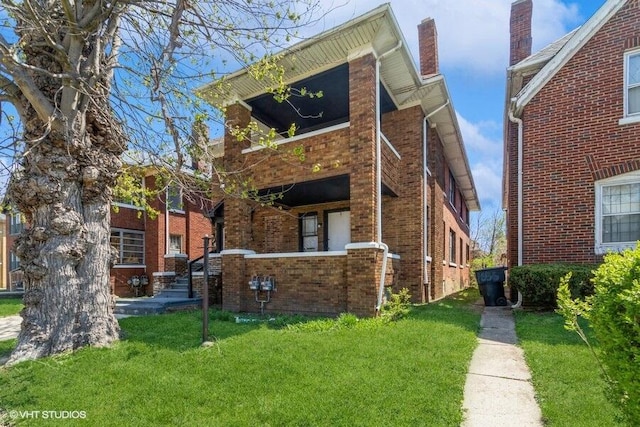 view of front facade featuring a chimney, brick siding, and a front lawn