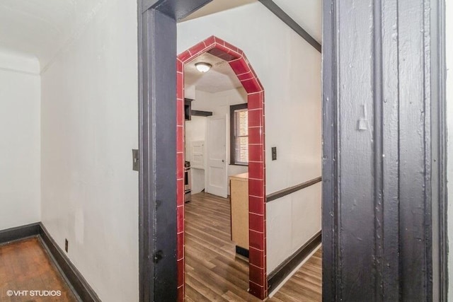 hall with baseboards, wood finished floors, and arched walkways
