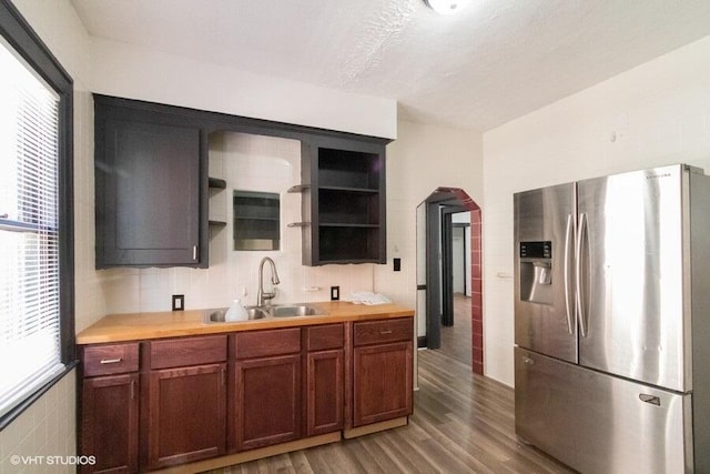 kitchen with wood finished floors, open shelves, stainless steel fridge with ice dispenser, backsplash, and a sink