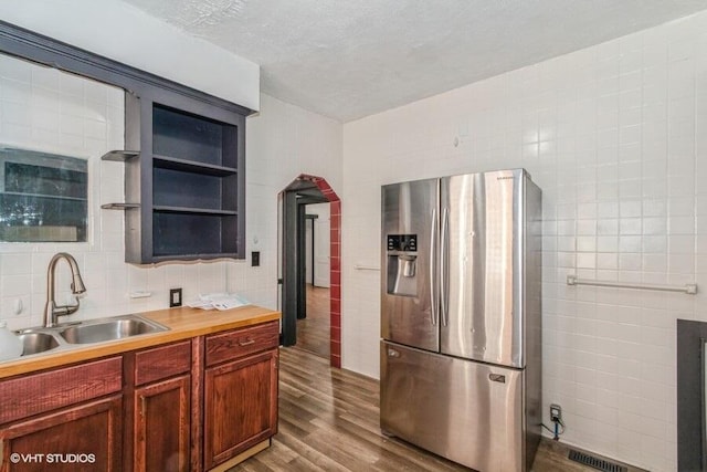 kitchen featuring open shelves, a sink, dark wood-style flooring, tile walls, and stainless steel refrigerator with ice dispenser