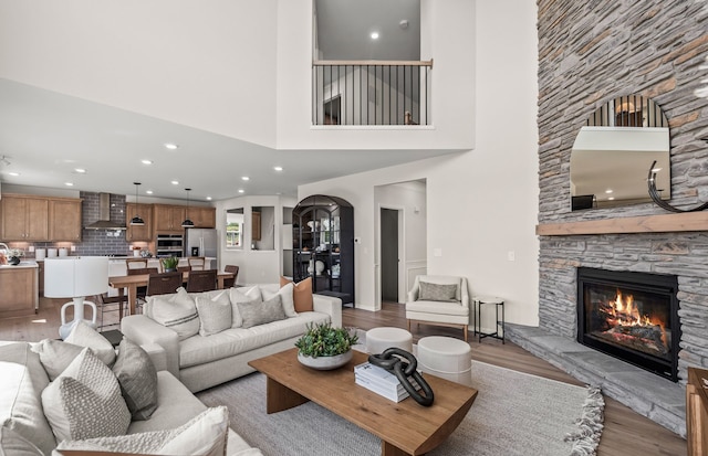 living room featuring recessed lighting, a towering ceiling, arched walkways, light wood-style floors, and a fireplace