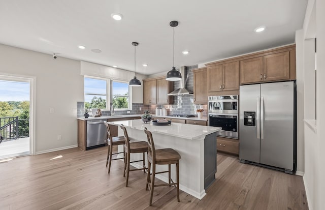 kitchen with a kitchen breakfast bar, backsplash, light wood-style floors, wall chimney exhaust hood, and appliances with stainless steel finishes