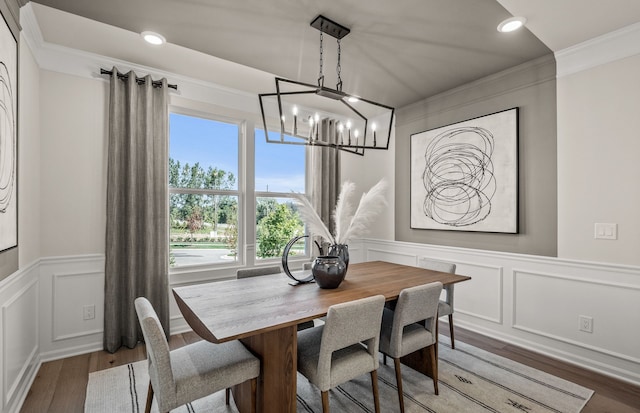 dining space featuring an inviting chandelier, wood finished floors, a decorative wall, crown molding, and wainscoting