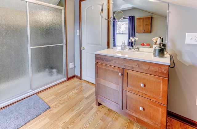 bathroom featuring wood finished floors, a shower with door, vanity, lofted ceiling, and baseboards