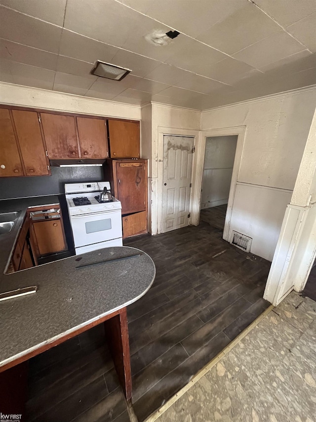 1048 Tremont Ave, Flint, MI 48505 - kitchen featuring white gas range, dark countertops, brown cabinets, under cabinet range hood, and a sink