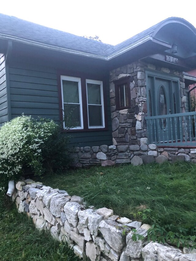 view of home's exterior with stone siding and a shingled roof