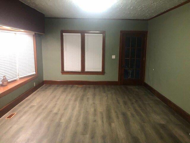empty room featuring a textured ceiling, wood finished floors, visible vents, and baseboards